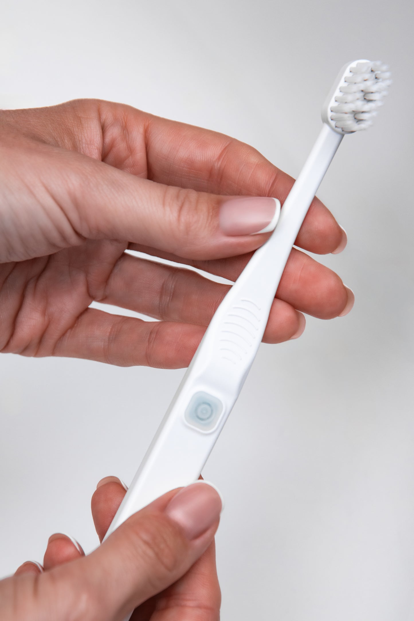 Moters rankoje laikomas Tromatz Mini bioelektrinis dantų šepetėlis šviesiame fone.
