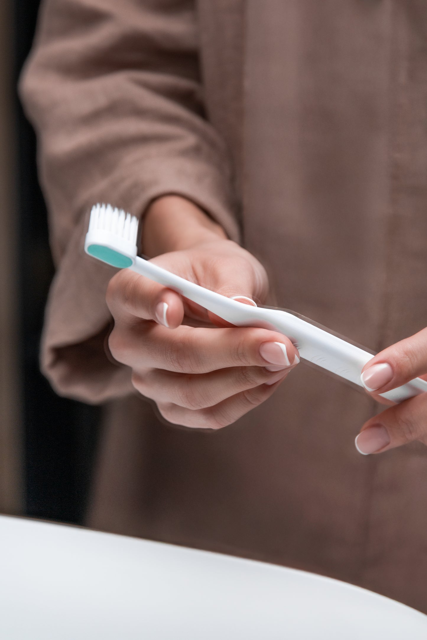 Lininiais drabužiais apsirengusi moteris vonios kambaryje laiko Tromatz Mini bioelektrinį dantų šepetėlį.