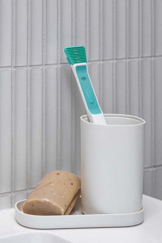 Žalias Tromatz bioelektrinis liežuvio valiklis – higienos priemonė sveikai burnos ertmei, baltame fone.