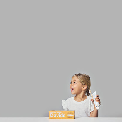 Davids Hydroxi™ balinamoji ir dantų emalį stiprinanti dantų pasta su nano hidroksiapatitu (apelsinų ir vanilės skonio), vaiko rankoje.