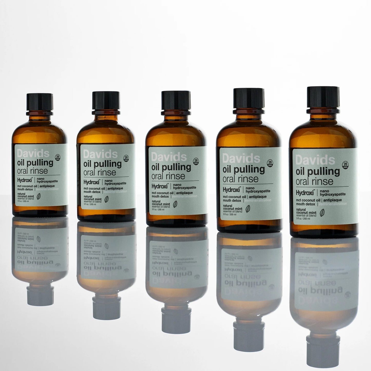 Davids Hydroxi™ burnos skalavimo skysčio aliejaus pagrindu buteliukai ant skaidraus paviršiaus su veidrodiniu atspindžiu.