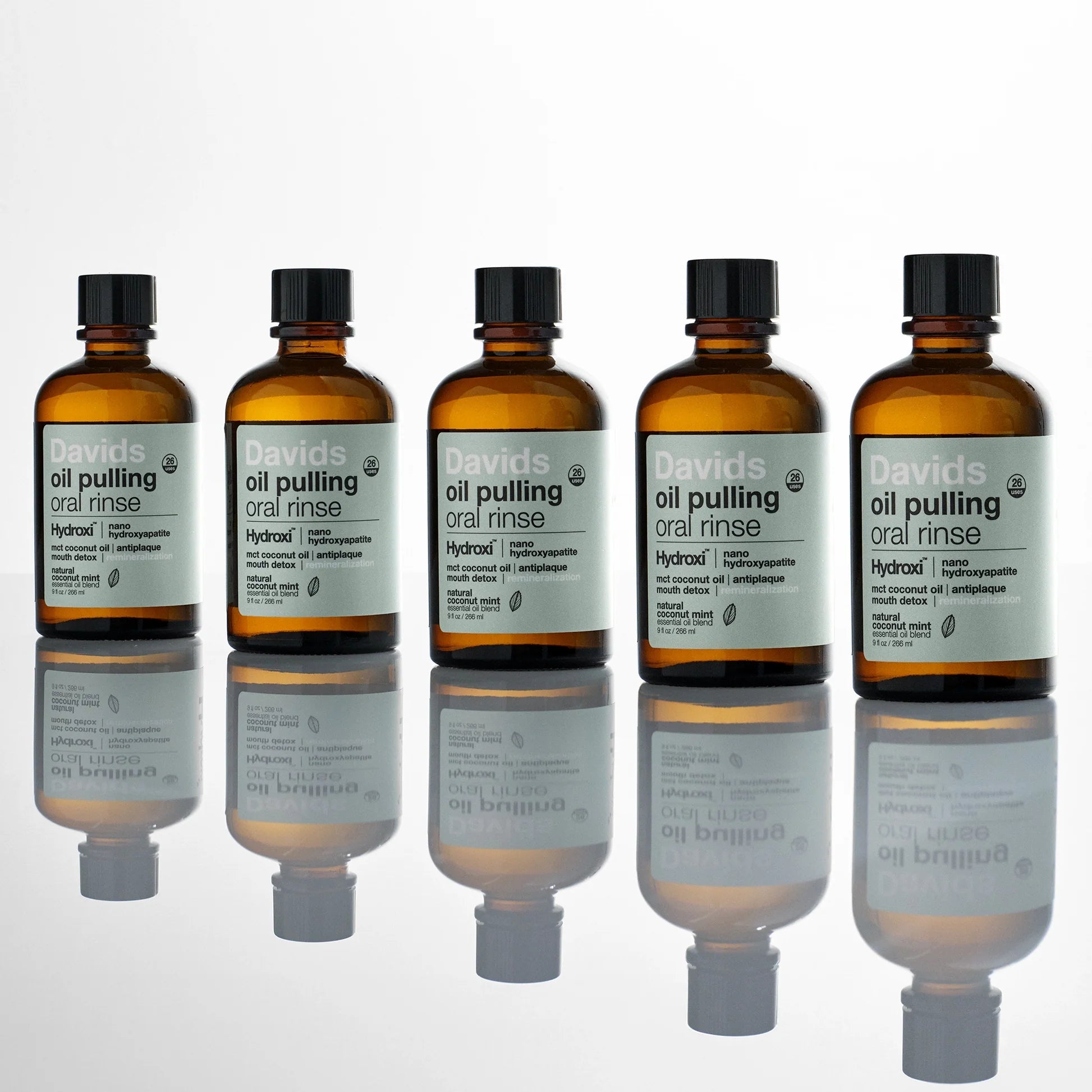 Davids Hydroxi™ burnos skalavimo skysčio aliejaus pagrindu buteliukai ant skaidraus paviršiaus su veidrodiniu atspindžiu.