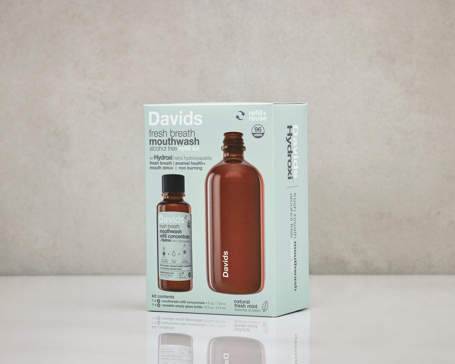 Davids Hydroxi natūralus burnos skalavimo skystis pakuotėje – rinkinys su daugkartinio naudojimo buteliu ir koncentratu ant stalo, pilkame fone