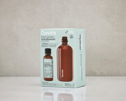 Davids Hydroxi natūralus burnos skalavimo skystis pakuotėje – rinkinys su daugkartinio naudojimo buteliu ir koncentratu ant stalo, pilkame fone