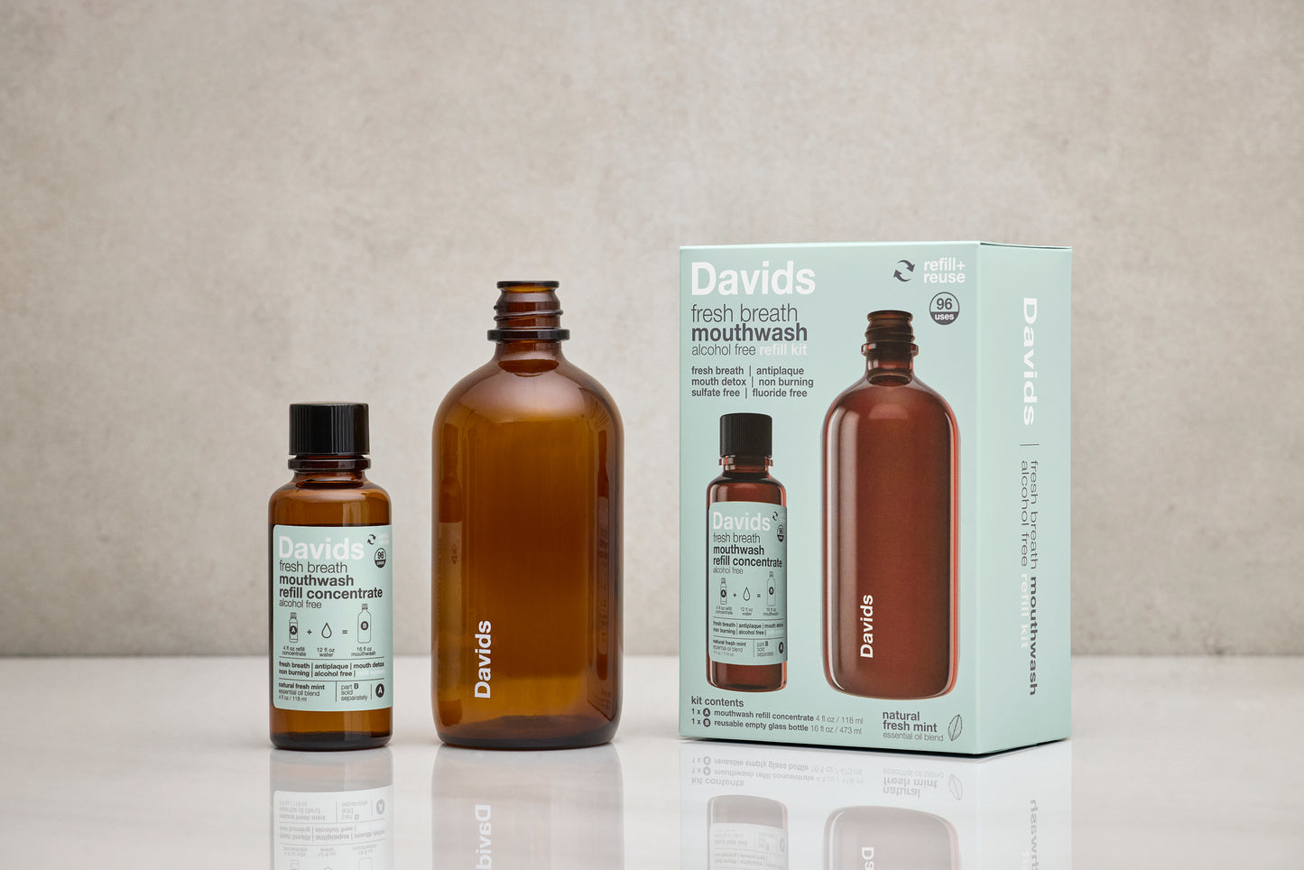 Davids Hydroxi natūralaus burnos skalavimo skysčio rinkinys ant stalo – daugkartinio naudojimo butelis, koncentratas ir pakuotė.