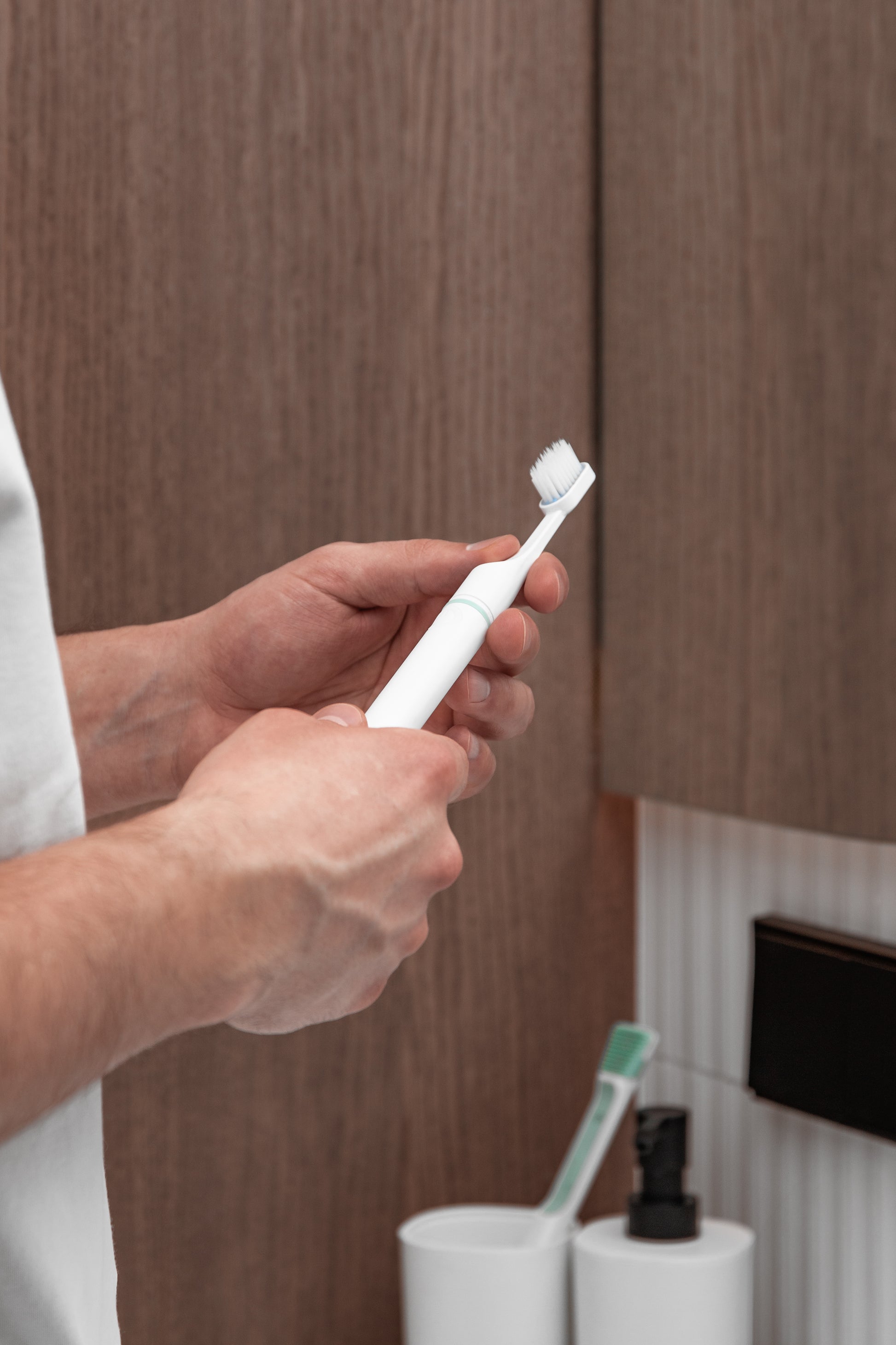 Tromatz bioelektrinis dantų šepetėlis vyro rankose, atvaizduotas vonios kambaryje.